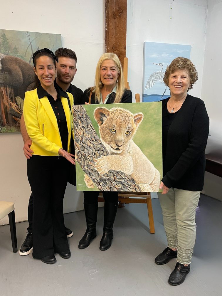 Four people posing with a painting of a lion cub in an art gallery.